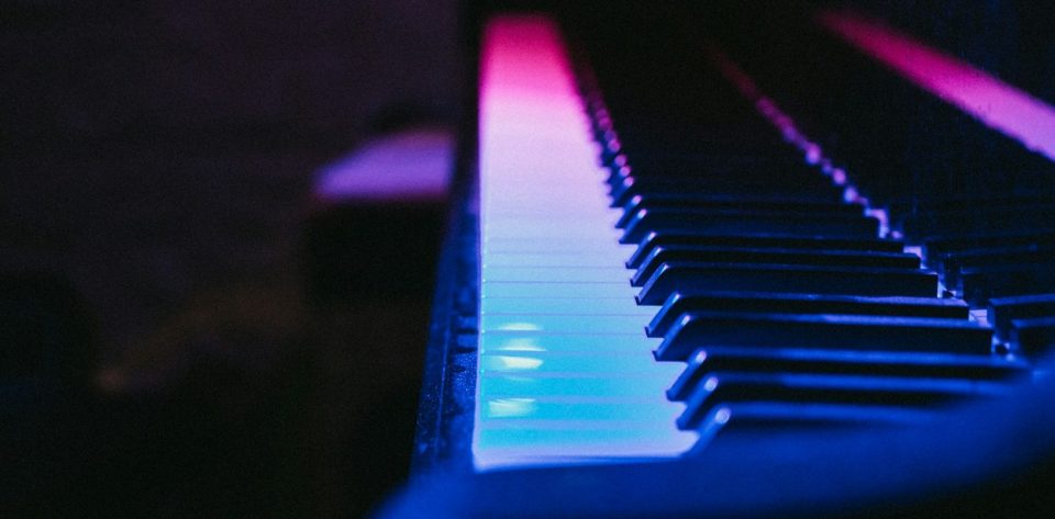 Nahaufnahme einer Klaviertastatur mit bunten Lichtern in Blau und Rosa.