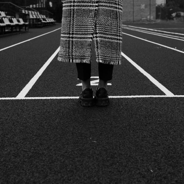 Person steht auf einer Laufbahn, blickt nach vorne, trägt einen karierten Mantel.