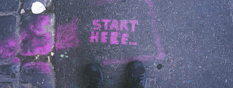 Schwarze Schuhe stehen neben einer lila Markierung mit der Aufschrift „START HERE“.
